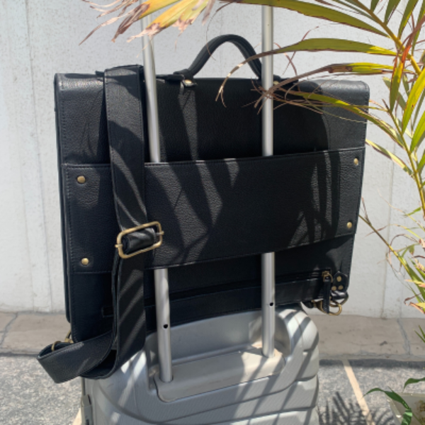 Black leather bag with gold hardware on a gray suitcase against a light-colored wall.