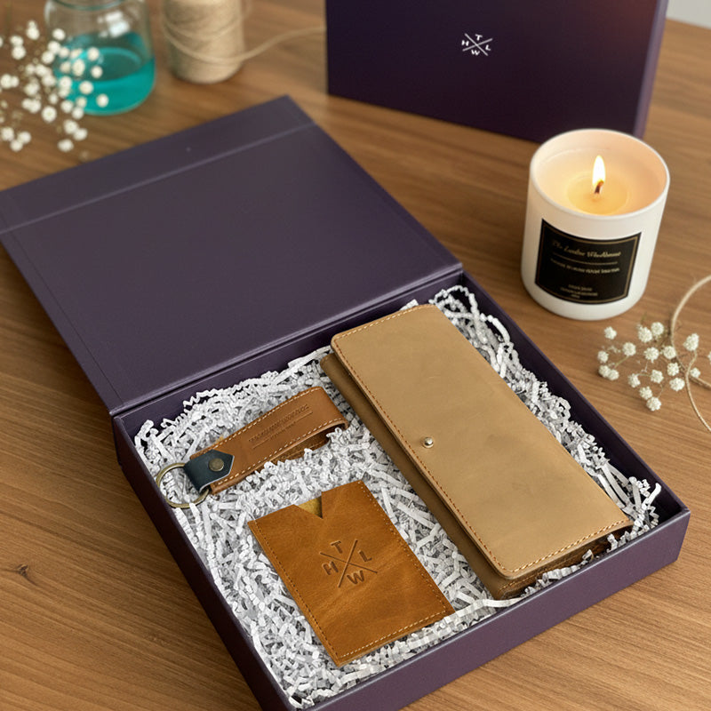 Brown leather wallet and cardholder set in a gift box with a candle keychain and decorative items on a wooden surface.