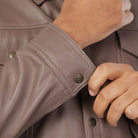 Close-up of a person adjusting the cuff of a brown leather jacket.