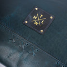 Close-up of a dark blue leather product with gold stitching and a logo patch.