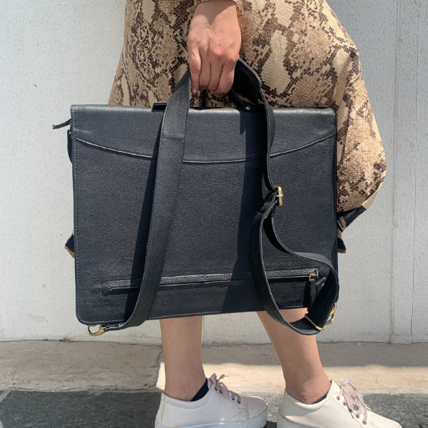 Person holding a black leather briefcase against a neutral background