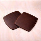 Two brown leather coasters on a light wooden surface