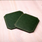 Two green hexagonal coasters on a light pink background