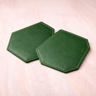 Two green hexagonal coasters on a light pink surface