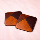 Two brown and black leather coasters on a light pink background