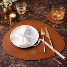 Dining setup with white plate, gold cutlery, and glasses on a brown placemat & coaster