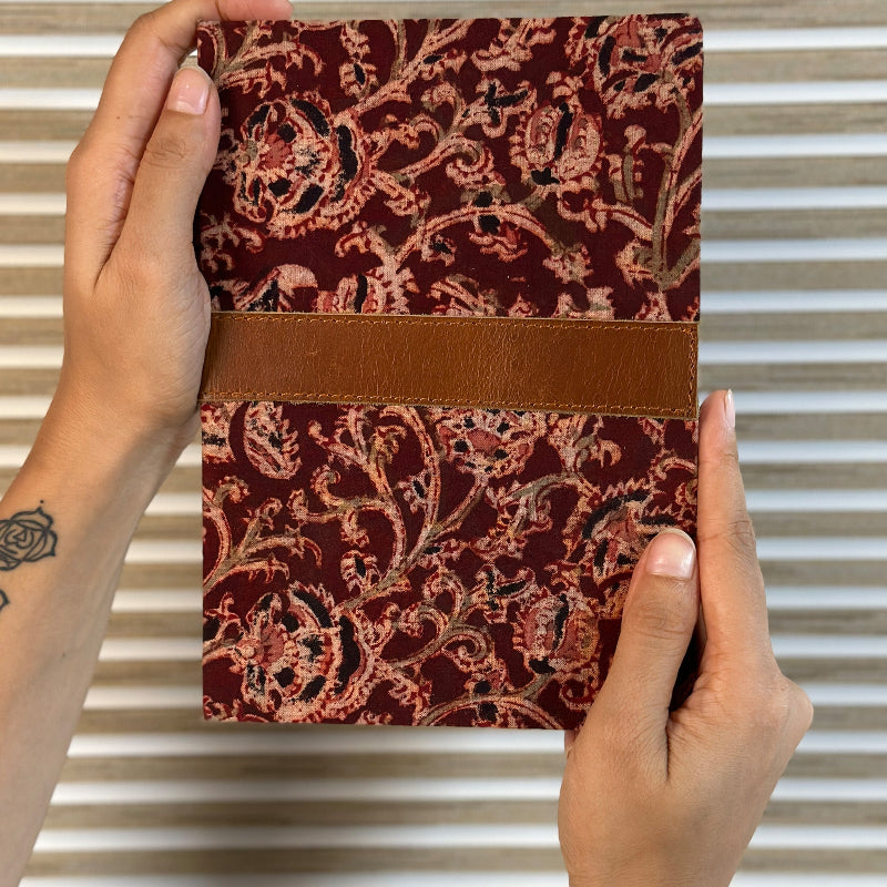 Hand holding a red patterned notebook with a brown band against a striped background
