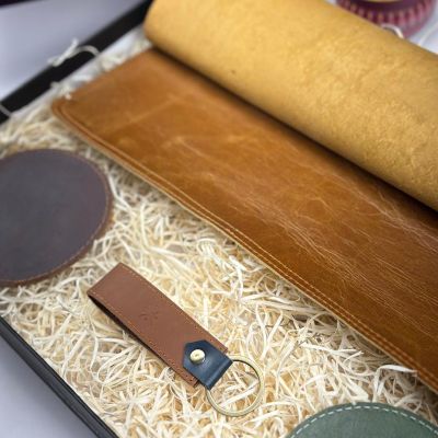 Brown leather desk mat and keychain on a bed of straw with a blurred background