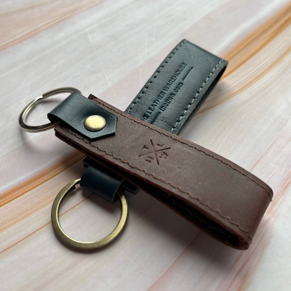Brown leather keychain with gold ring on a light wooden surface