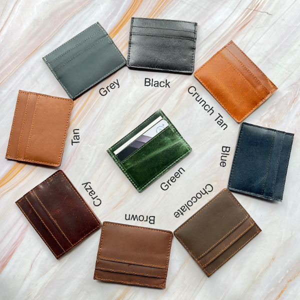 Collection of leather card holders in various colors on a light wooden surface.