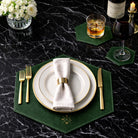 Dining table setting with white plates, gold cutlery, and green placemats and coaster on a black marble surface.
