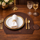 Elegant table setting, placemat & coasters with gold and white cutlery, plate, and napkin on a wooden table.