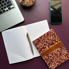 Open notebook with pen, decorative notebook, laptop, and phone on a purple surface