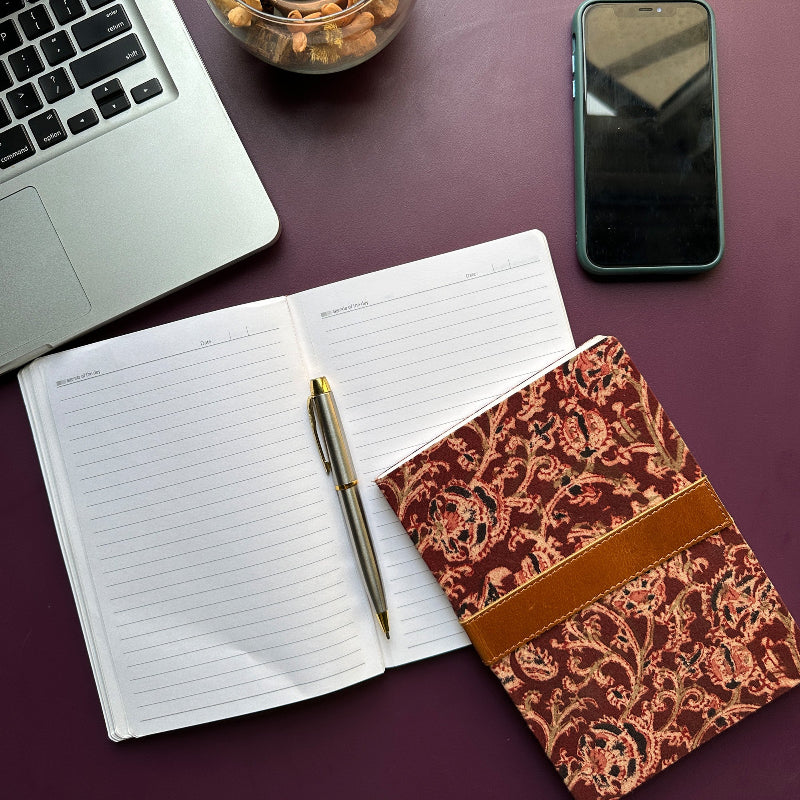 Open notebook with pen, decorative notebook, laptop, and phone on a purple surface