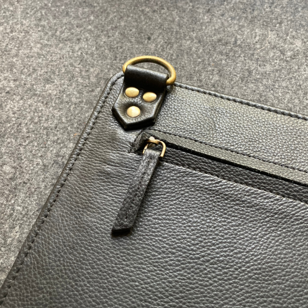 Close-up of a black leather pouch with gold zipper pulls on a gray textured background