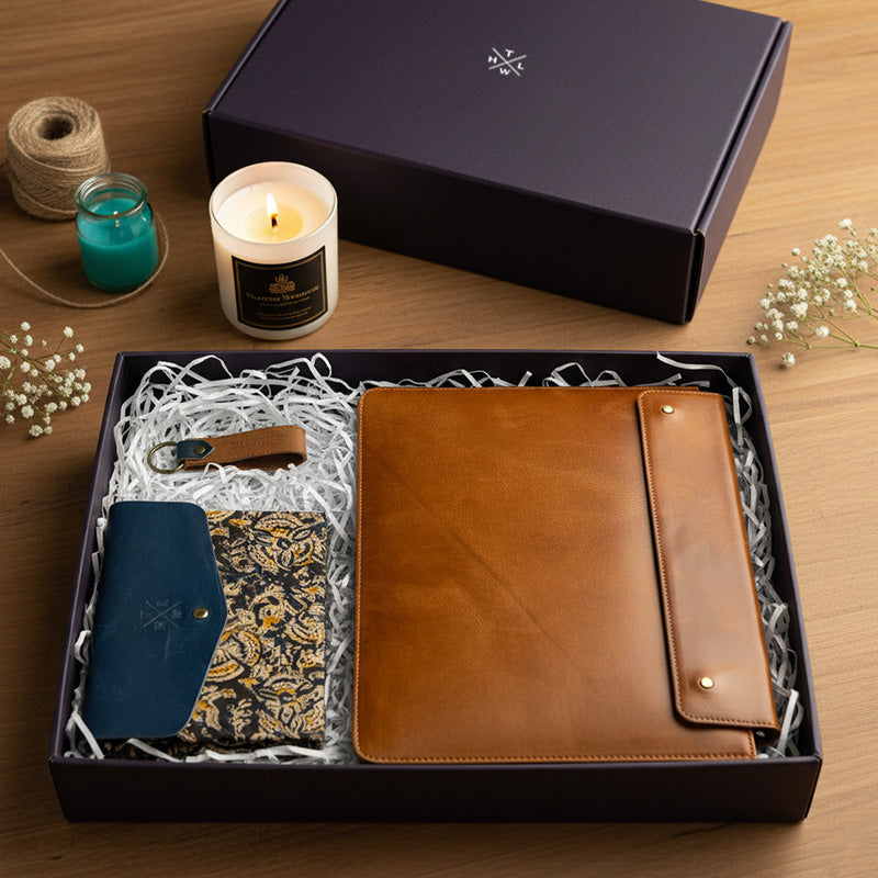 Leather corporate gift box with tan folder, blue wallet, and keychain beside a lit candle.