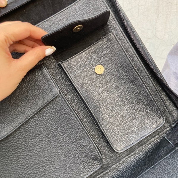 Close-up of a person opening a black leather bag with gold buttons.