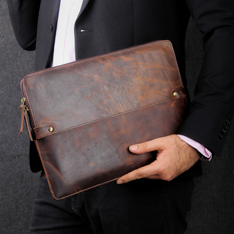 Man in a black blazer holding a premium brown leather laptop sleeve with a rustic finish.