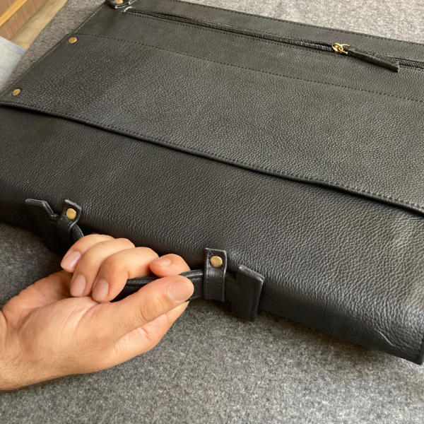 Person adjusting a black leather bag strap on a gray surface