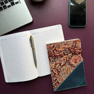Open notebook with a pen, decorative notebook, laptop, and phone on a dark surface