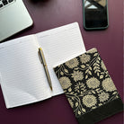 Open notebook with a pen, floral-patterned cover on a dark surface