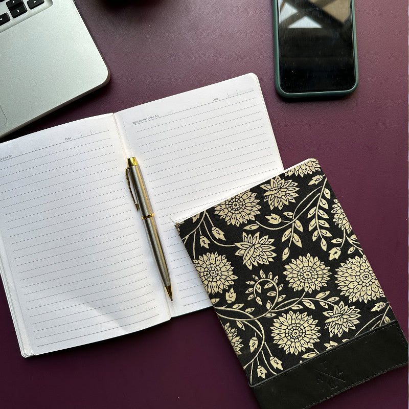 Open notebook with a pen, floral-patterned cover on a dark surface