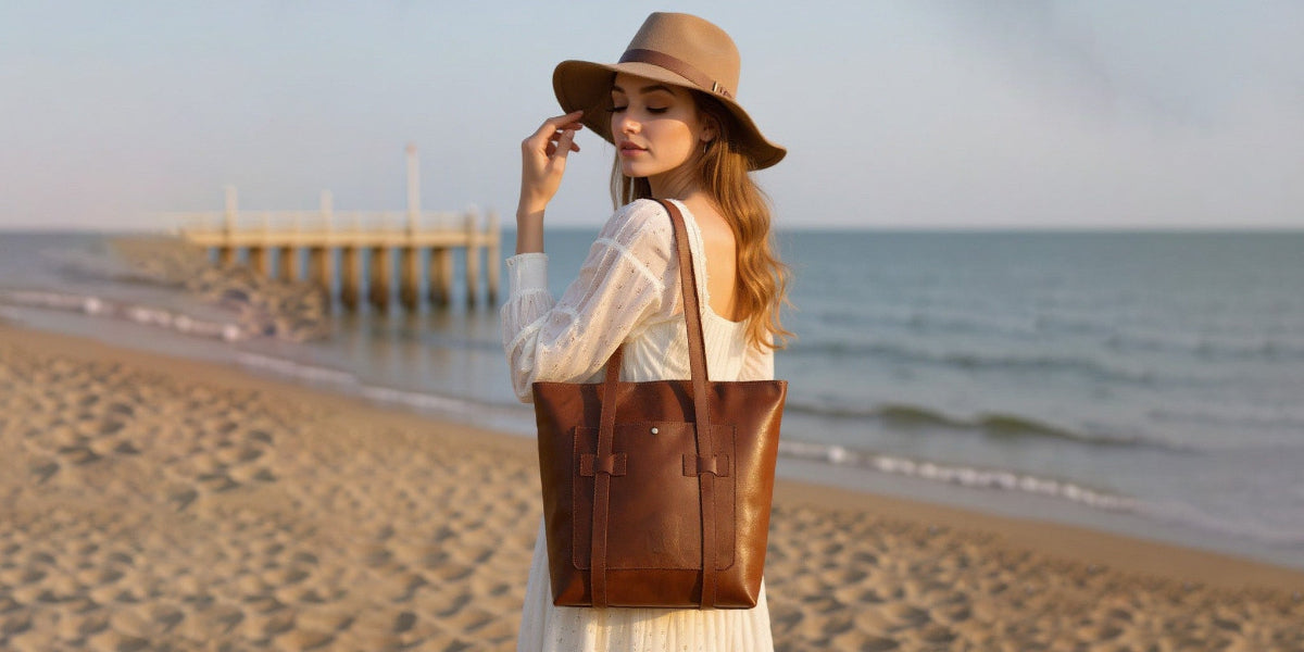 Woman on a beach wearing a brown hat and carrying a large brown leather tote bag.