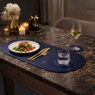 Dining table setup with a plate of food, wine glass, and water glass on a blue placemat and coaster