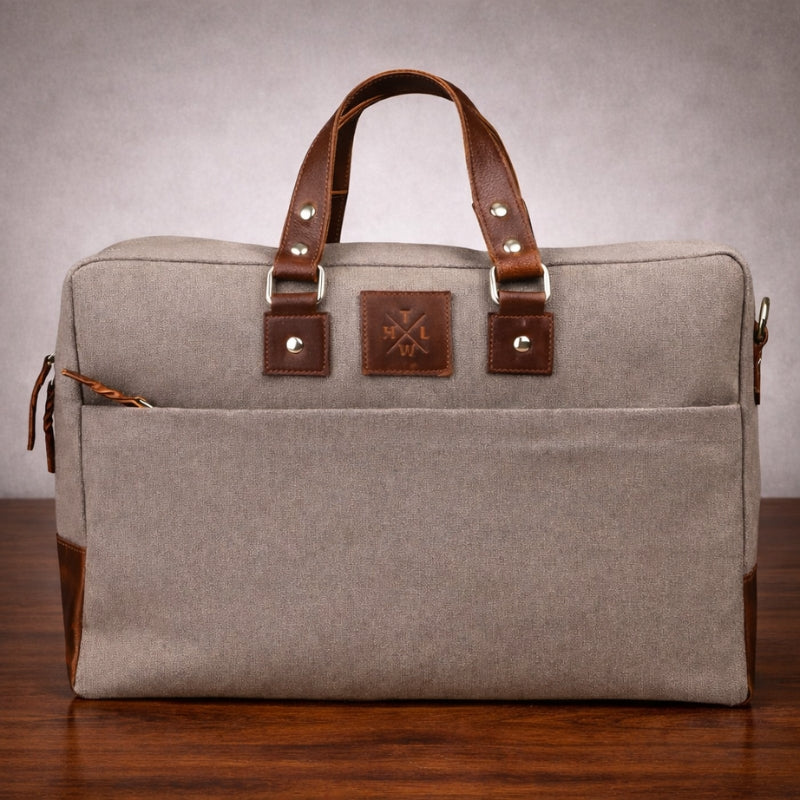 Gray bag with brown canvas & leather straps on a wooden surface
