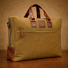 Brown leather and canvas bag with brown leather straps on a wooden surface.