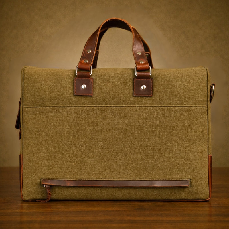 Green canvas briefcase with brown leather straps on a wooden surface and brown background