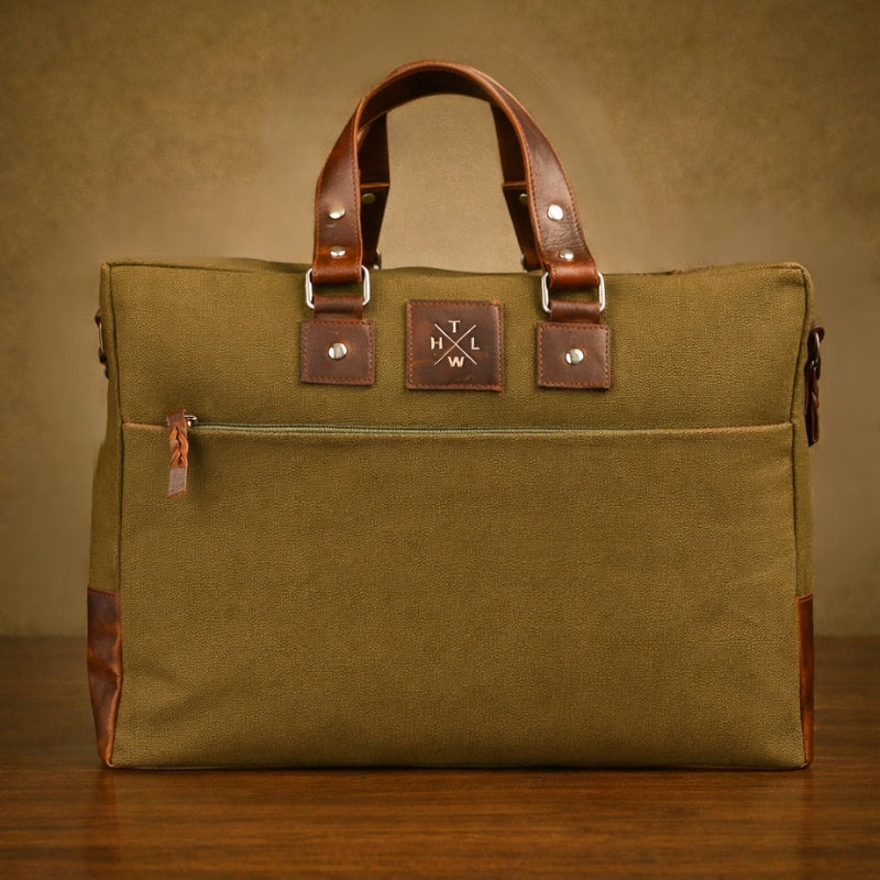 Green canvas bag with brown leather handles and trim on a wooden surface.