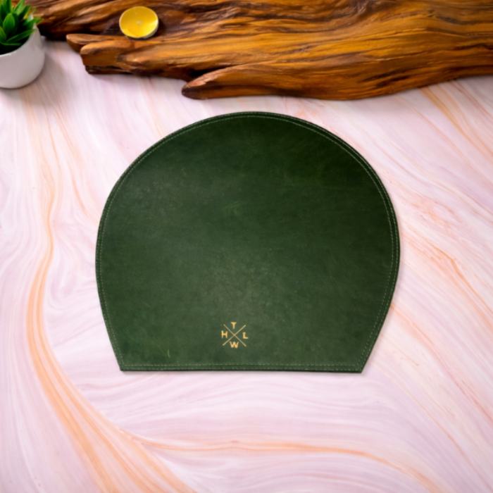 Green half moon placemat with a logo on a light pink surface with a wooden log and plant in the background