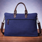 Blue canvas bag with brown handles and straps on a wooden surface back view.