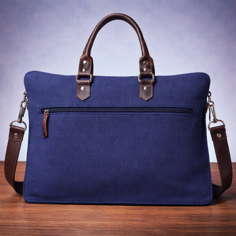 Blue canvas bag with brown handles and straps on a wooden surface back view.