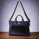 Blue canvas laptop bag with brown with strap on a wooden surface with a blue background