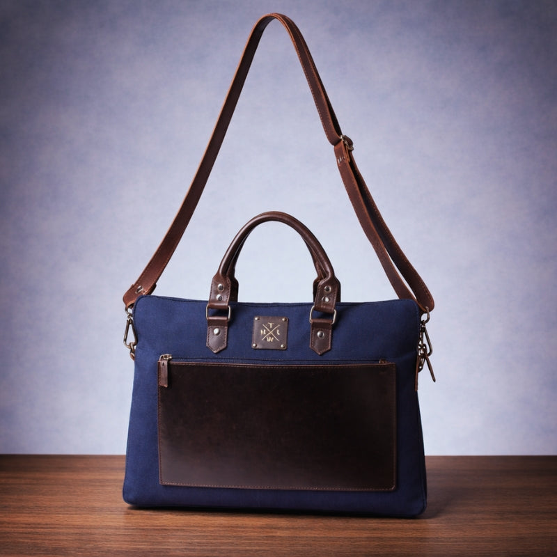 Blue canvas laptop bag with brown with strap on a wooden surface with a blue background