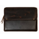 A dark brown distressed leather laptop sleeve with a front flap pocket, brass snap buttons, and a small embossed logo, shown flat on a white background.