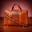Brown leather briefcase with a shoulder strap on a wooden surface