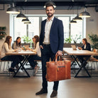 Man in a suit holding a brown leather briefcase in an office setting with colleagues at tables.