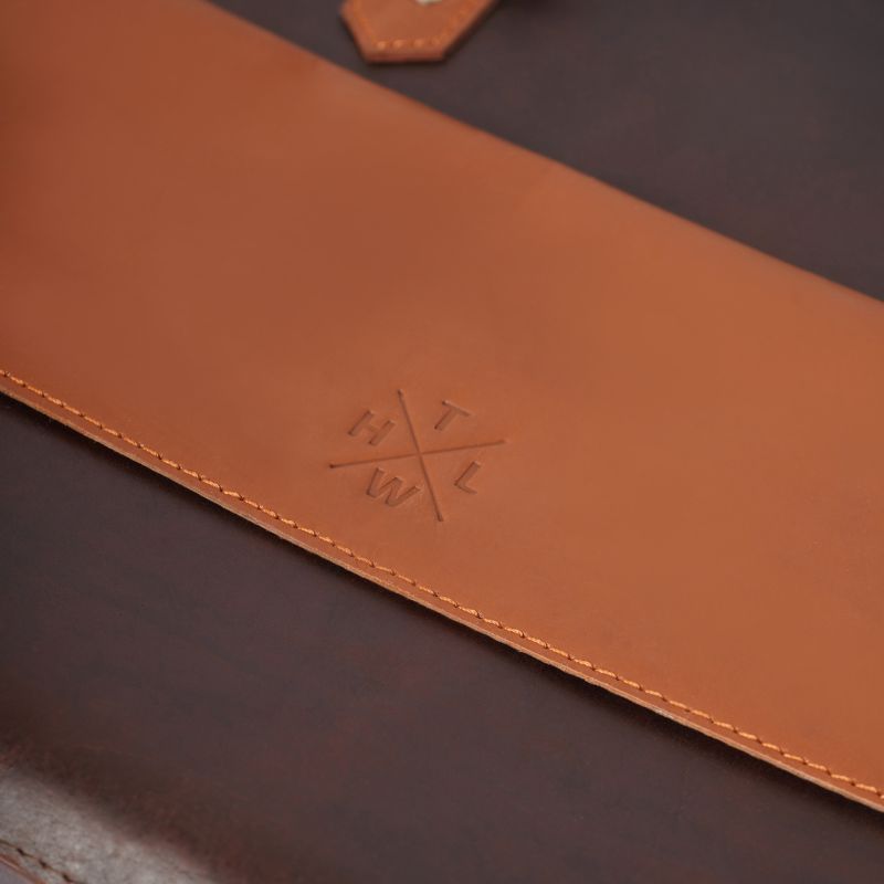 Close-up of a brown leather laptop bag 
with a logo on a dark background