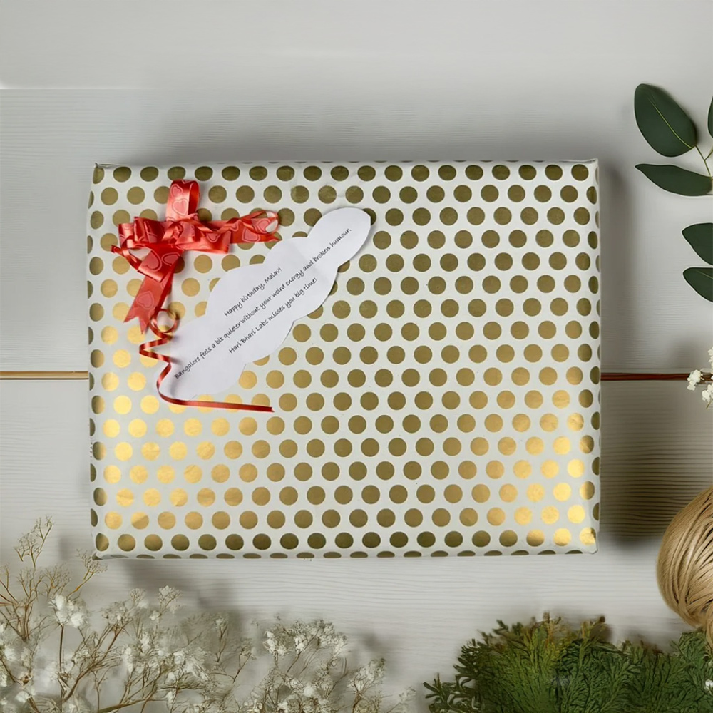 Gift box with gold polka dot pattern, red ribbon, and white card on a light wooden surface.