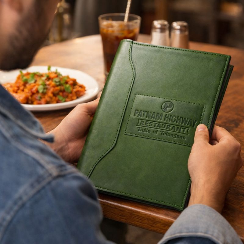 Person holding a green menu with 'Fatham Highway Restaurant' logo at a dining table.