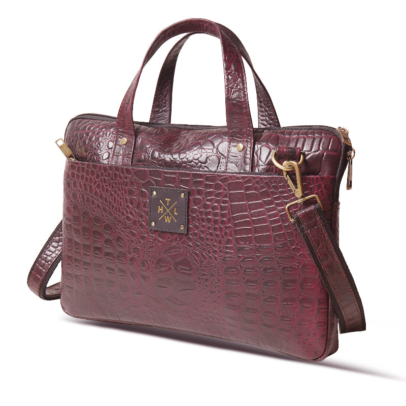 Maroon crocodile-patterned handbag with gold hardware on a white background