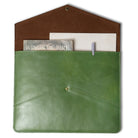 Green leather pouch with a brown flap containing a book and pen on a white background