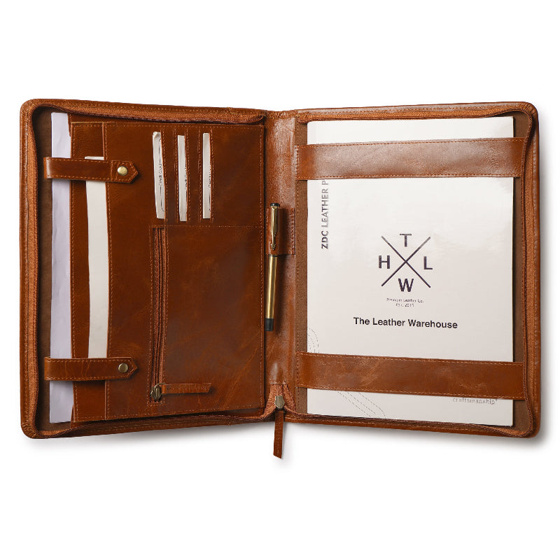 Open brown leather portfolio folder with multiple compartments, card slots, a zippered pocket, pen holder, and A4 documents inside, branded with 'The Leather Warehouse'.