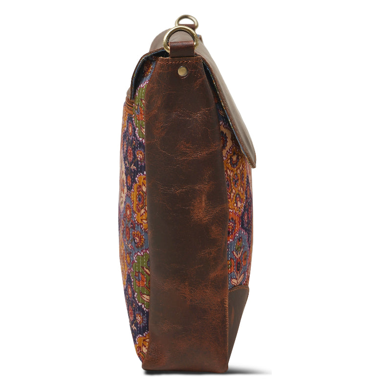 Brown leather handbag with intricate patterned flap on a white background