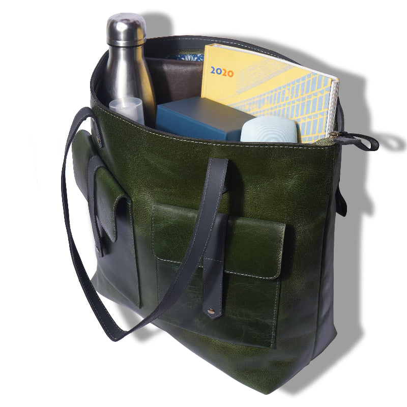 Green leather tote bag with various items on a white background