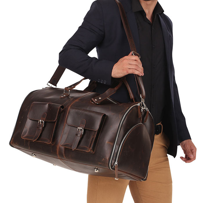 Man carrying a dark brown genuine leather travel duffle bag with shoulder strap, featuring front buckle pockets, styled with formal outfit for business or weekend travel.