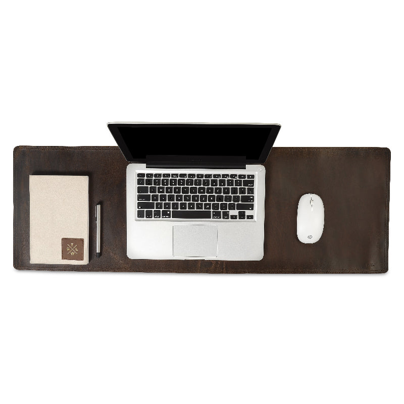 Laptop on a large dark brown desk pad with a mouse and small notepad on a white background
